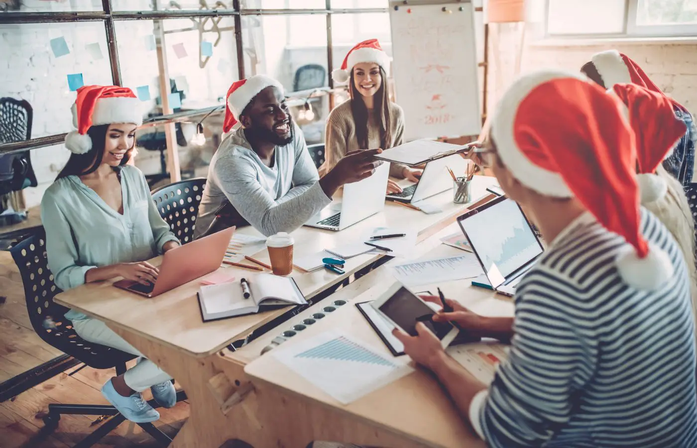 Groupe de collègues portant des bonnets de Noël, travaillant ensemble dans un bureau décoré pour les fêtes, illustrant la convivialité et l’esprit d’équipe.